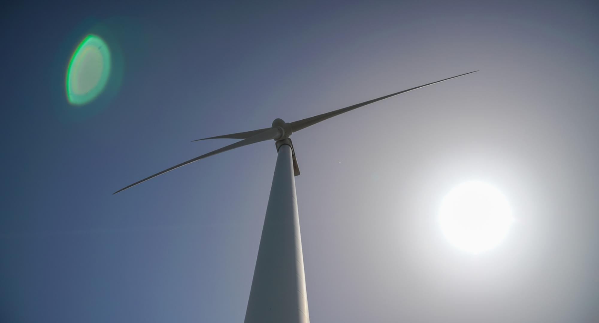 Wind turbine from below, with a blue sky behind it