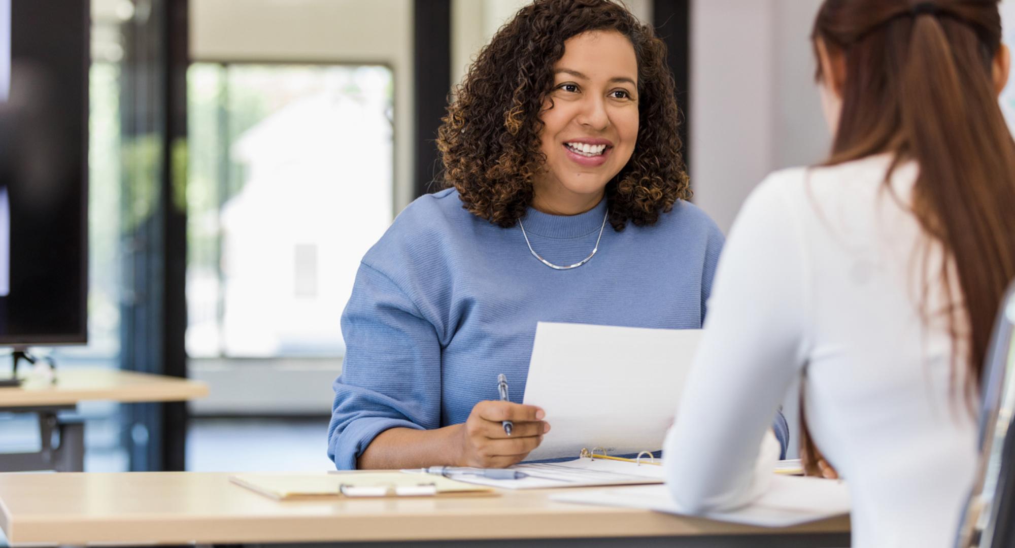 The office manager holds onto a resume while speaking with the new intern they are considering.