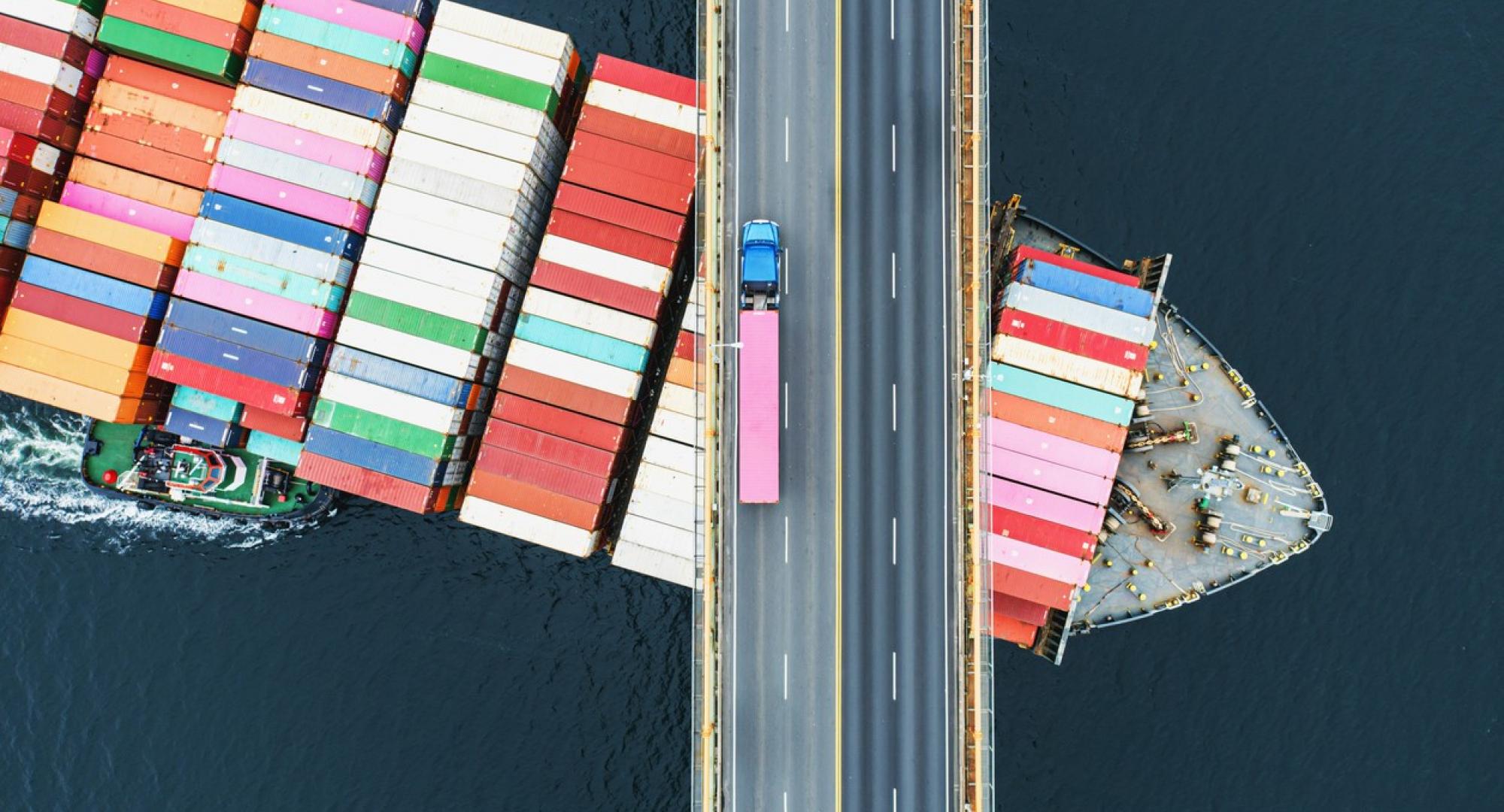 Big freight ship passing under a road bridge with a truck on it