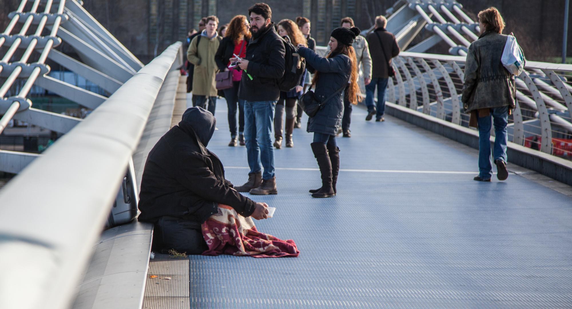 Homeless person surrounded by tourists on a bridge in London