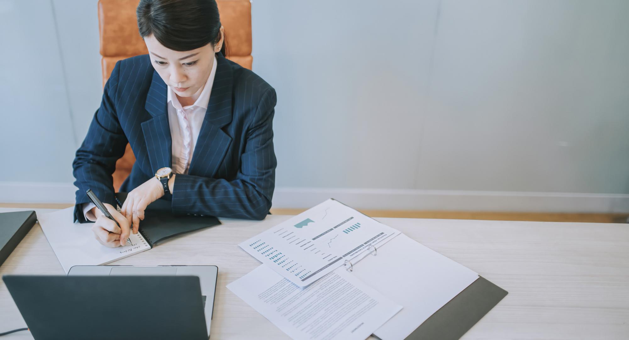 Woman working on a laptop with papers on the desk in front of her