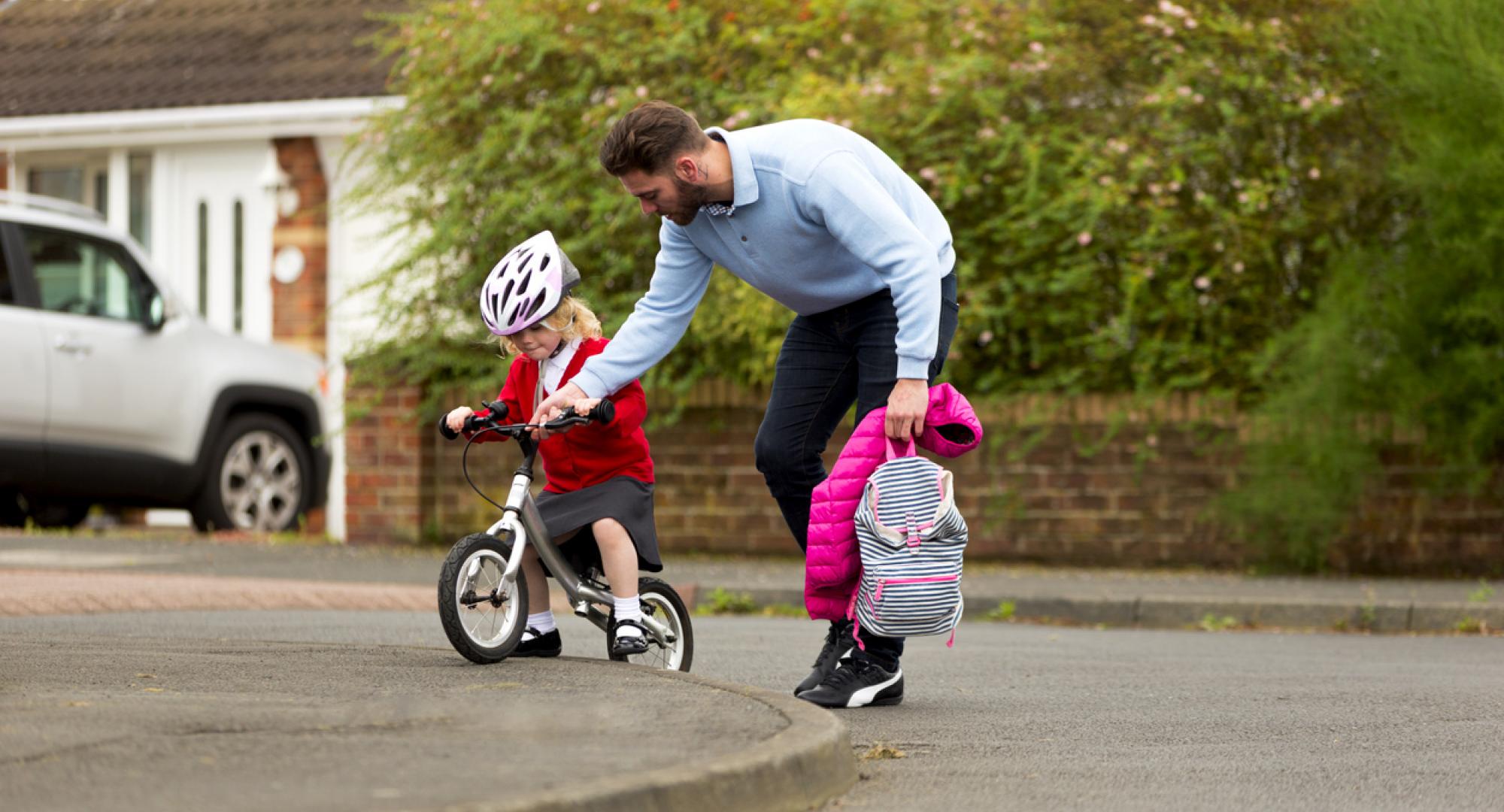 Dad helping his daugher cycle to school