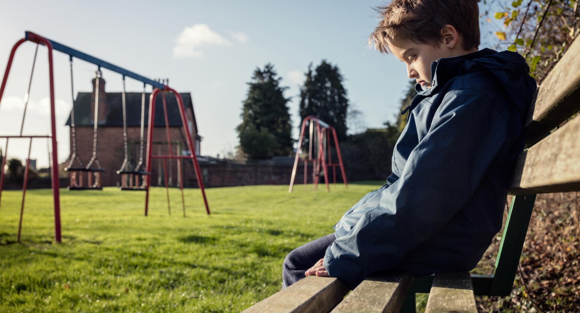 Lonely child sitting on play park playground bench