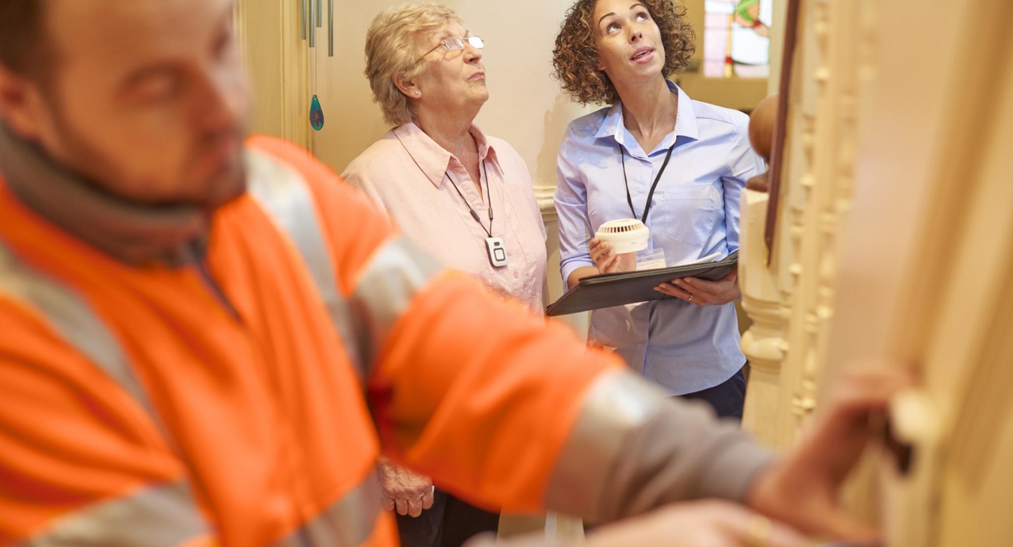 an alarm fitter fits an alarm in a senior woman's house