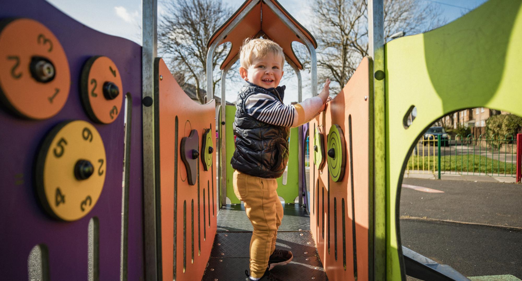 Young boy playing at a public park on a climbing frame on a sunny day