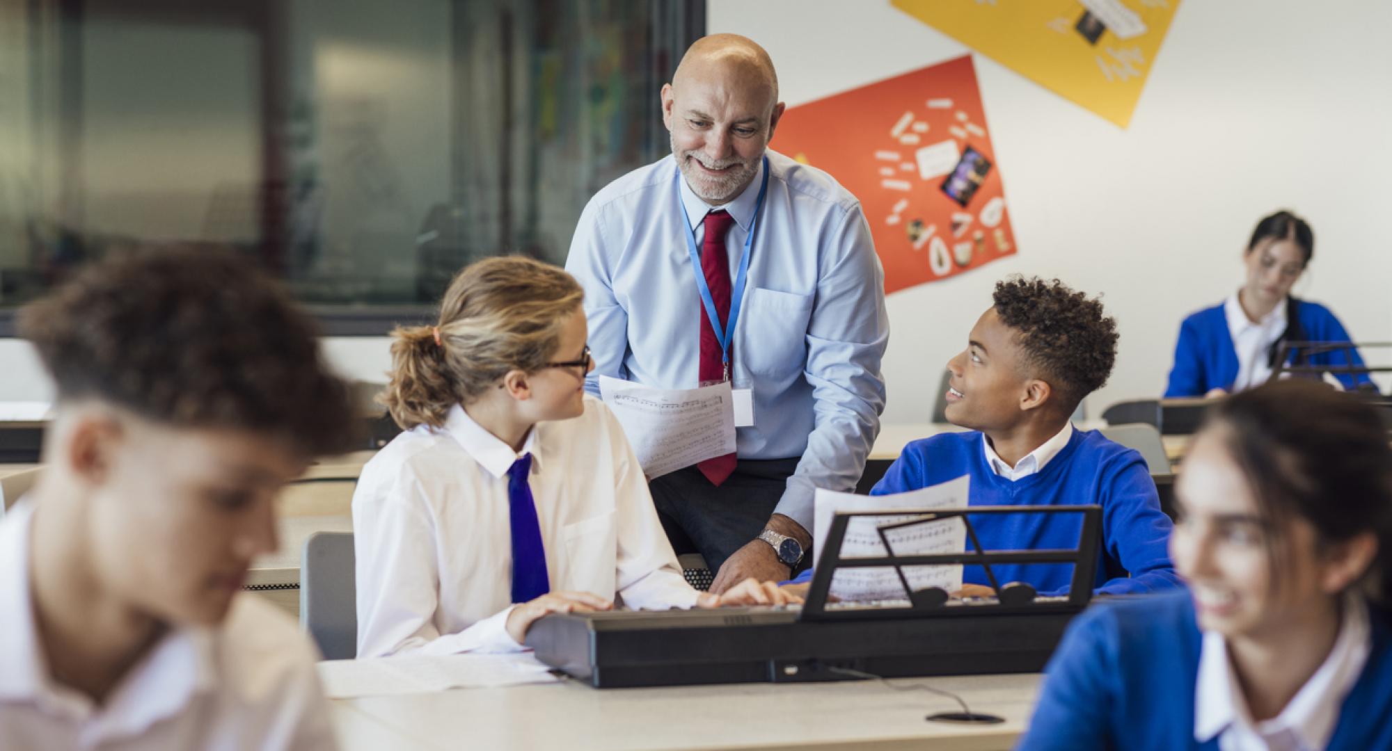 front-view shot of teenage music students in a classroom learning how to play the keyboard with their teacher at a school