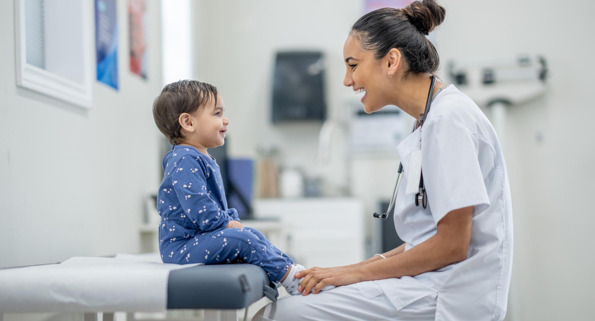 A sweet little toddler sits up on an exam table in a doctors office as her female doctor conducts a routine check-up.