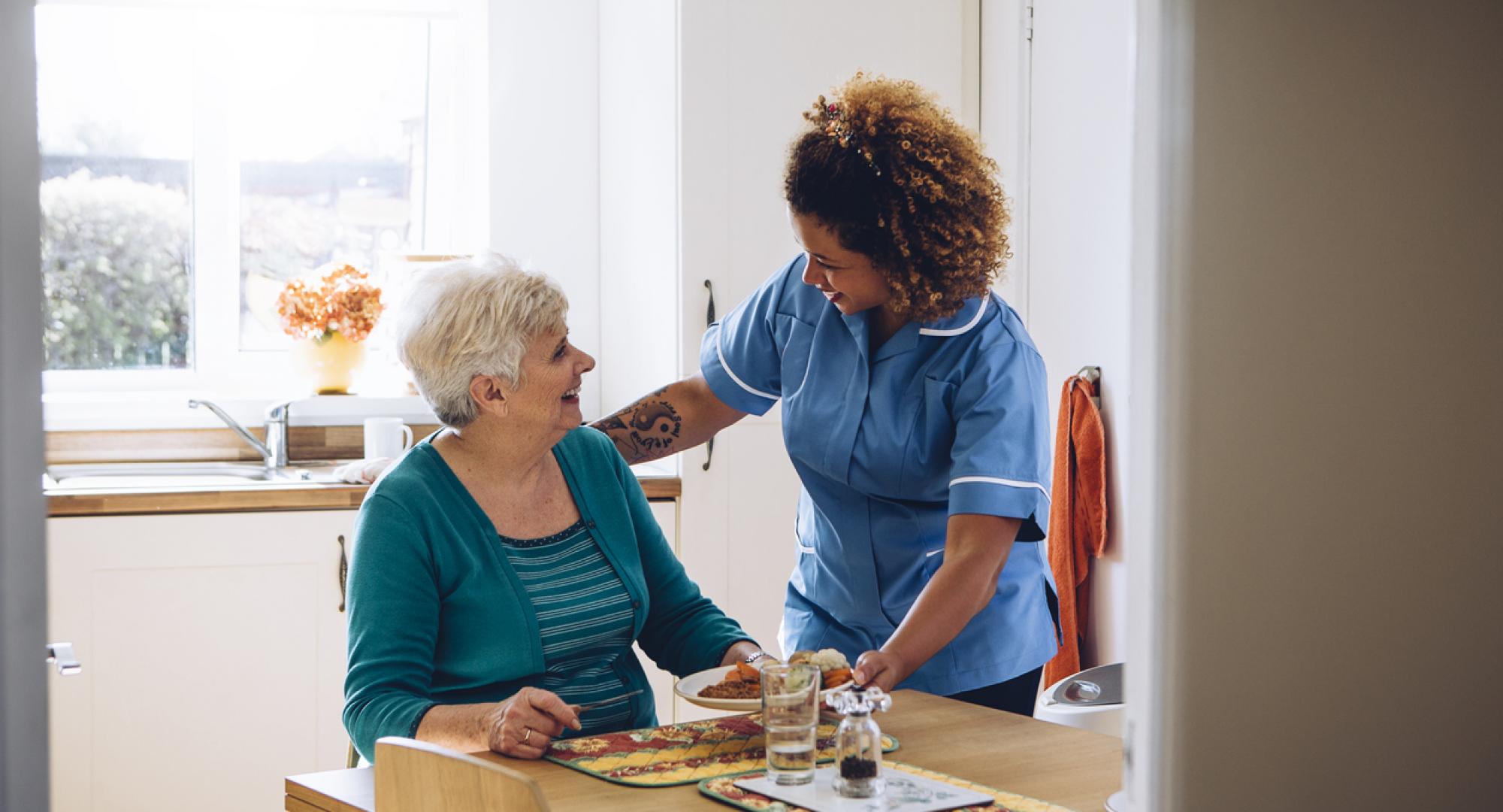 Care worker giving an old lady her dinner in her home.