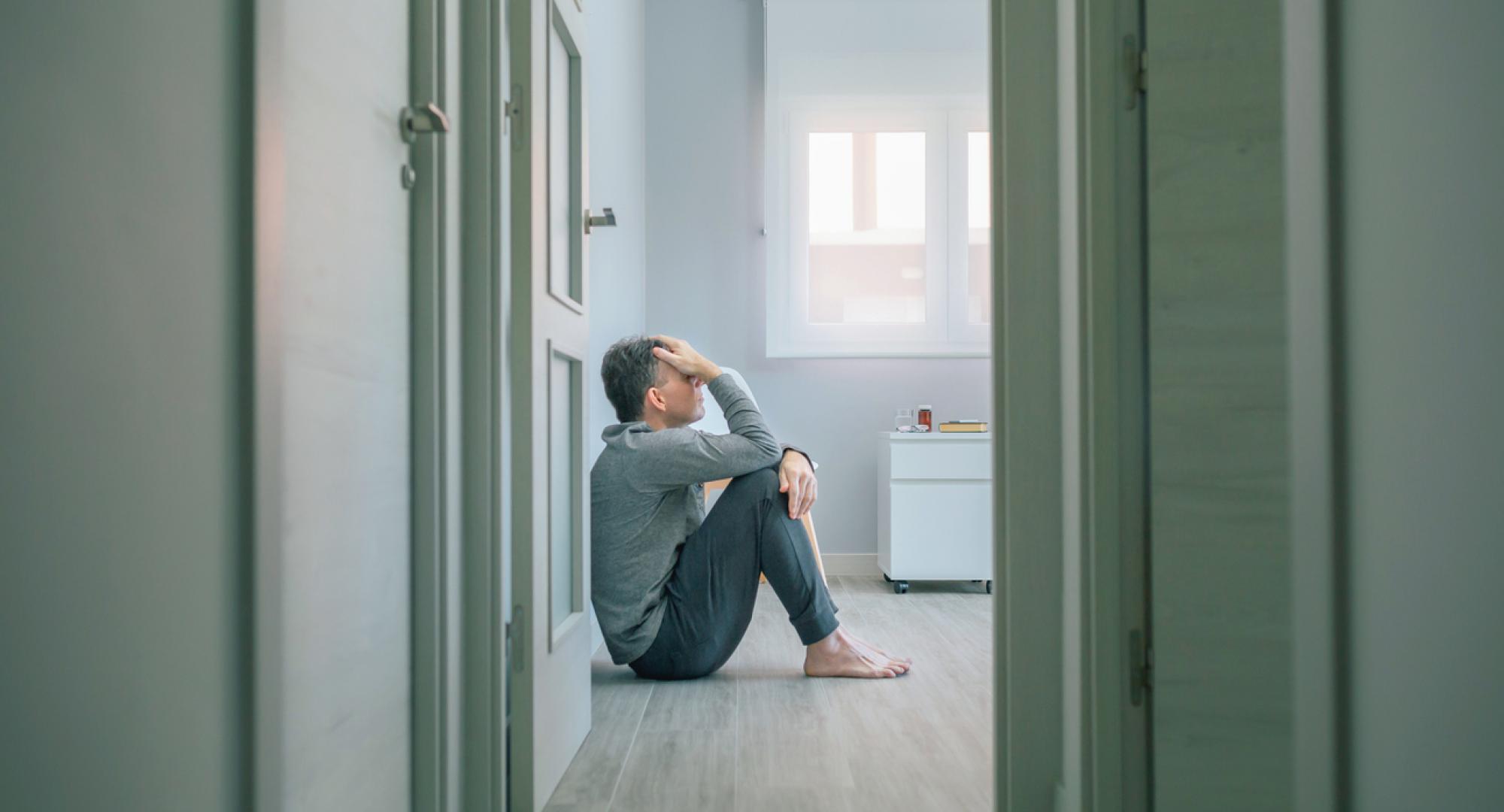 Desperate man with suicidal thoughts holding his head with hand sitting on the floor