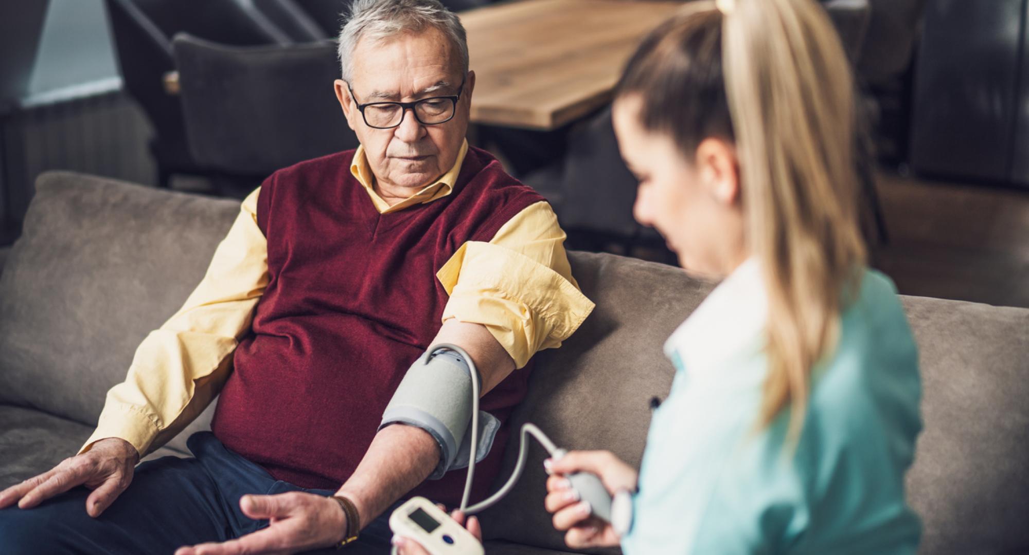 Home doctor is measuring blood pressure of old man at his home