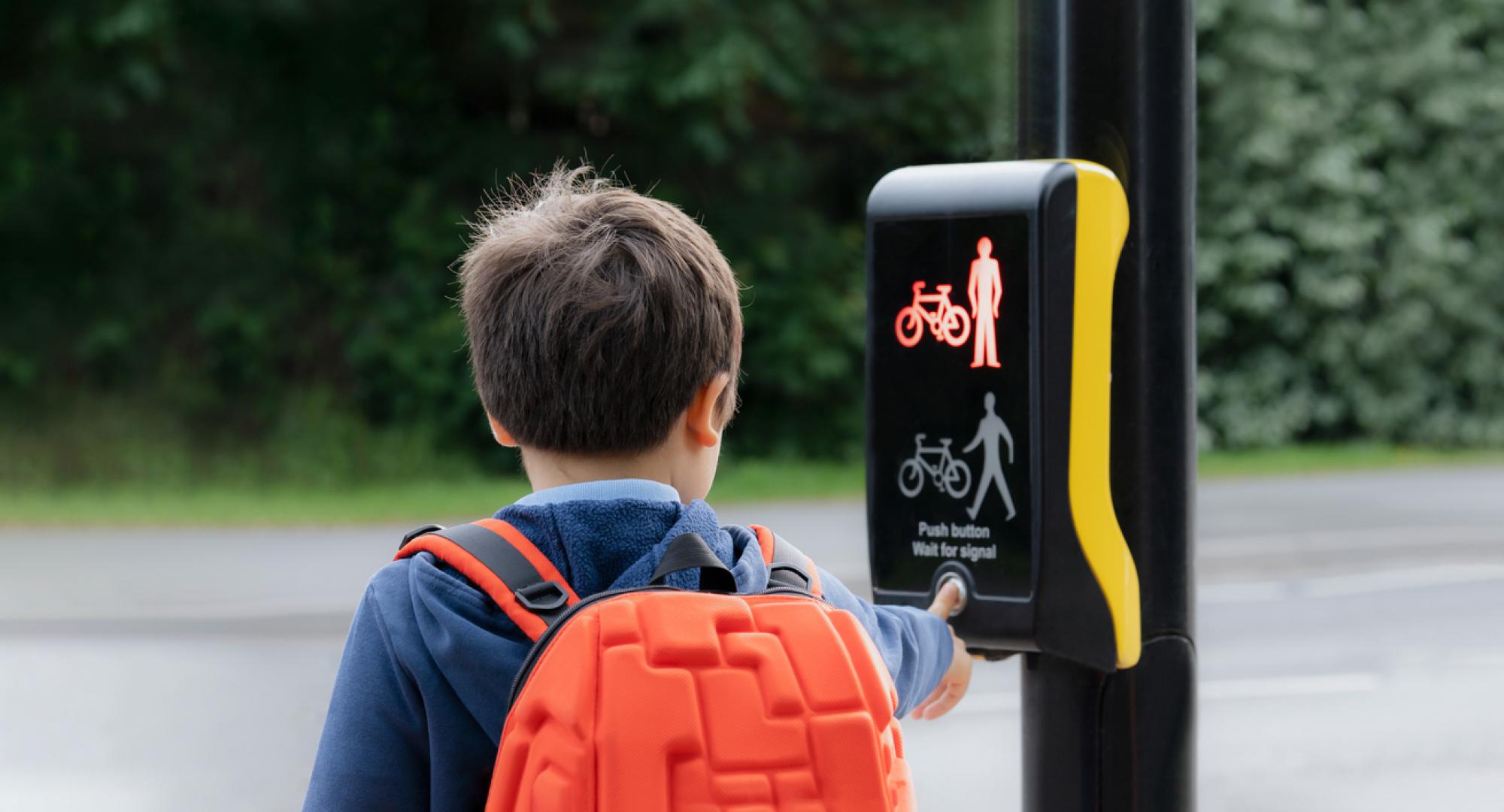 School kid pressing a button at traffic lights on pedestrian crossing on way to school