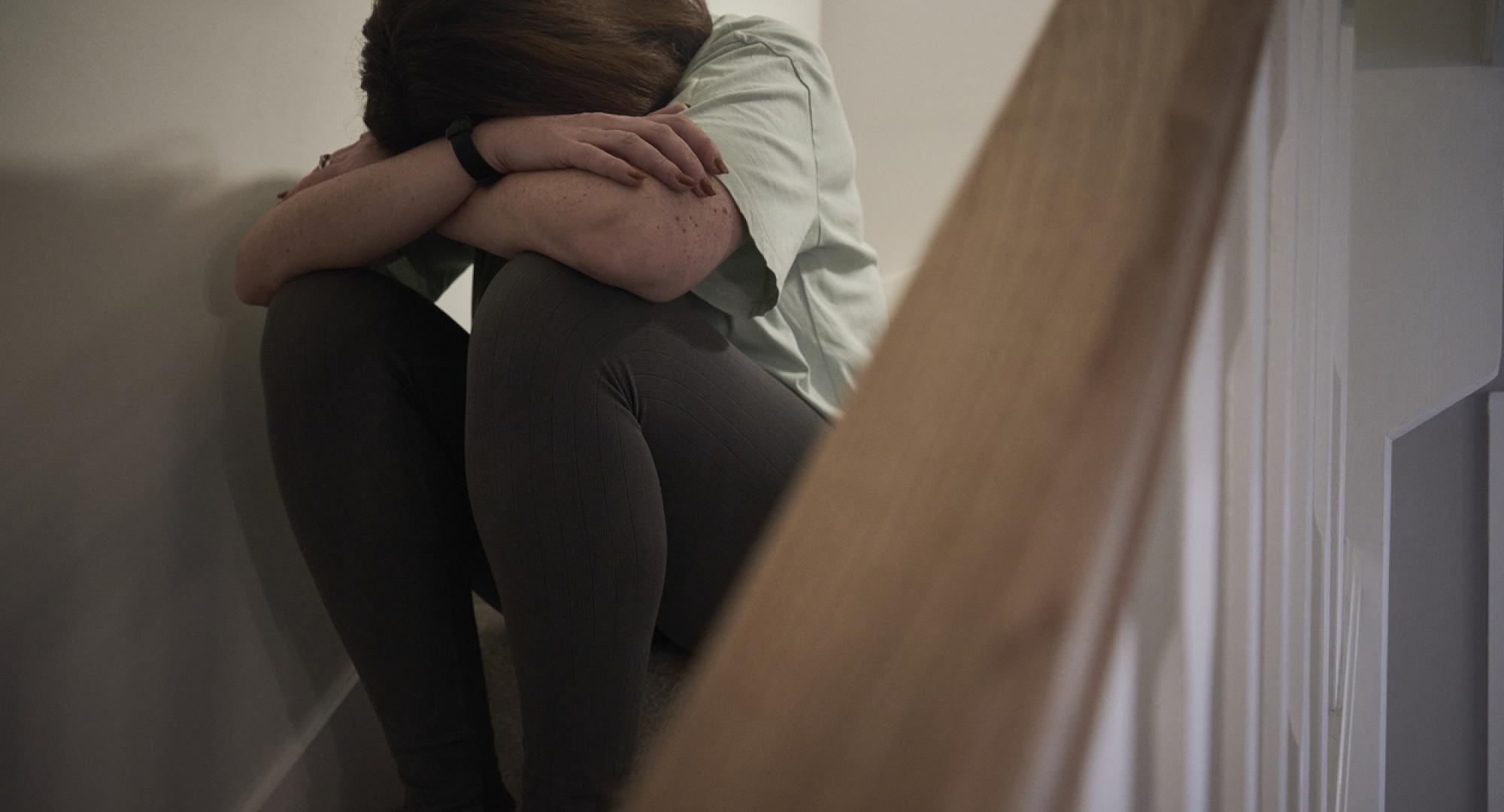 A woman suffering from depression or domestic abuse sat on the stairs of her home hiding her face.