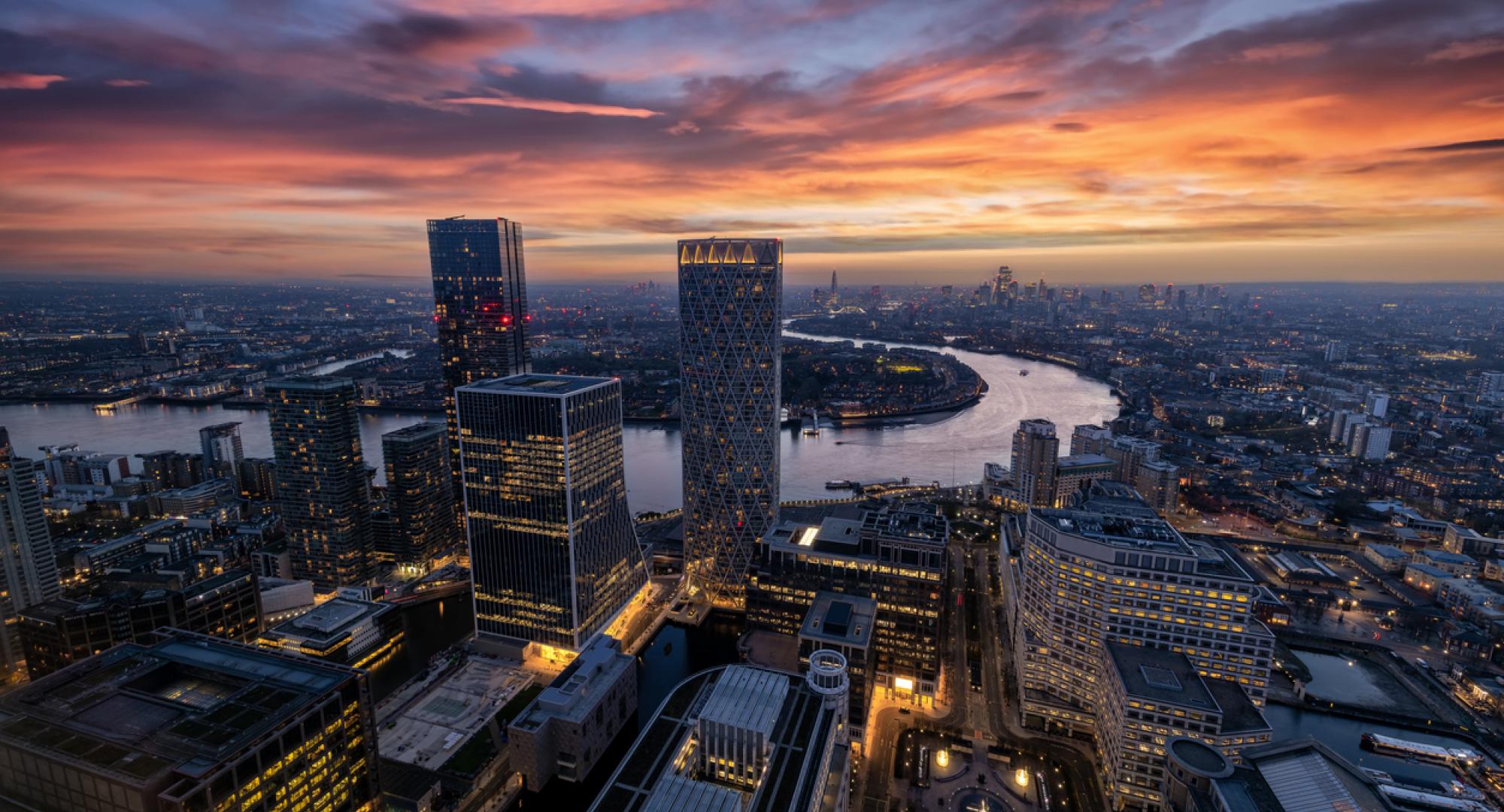 Panoramic view through the modern skyscrapers of Canary Wharf of the illuminated London skyline and Thames river during dusk time, England