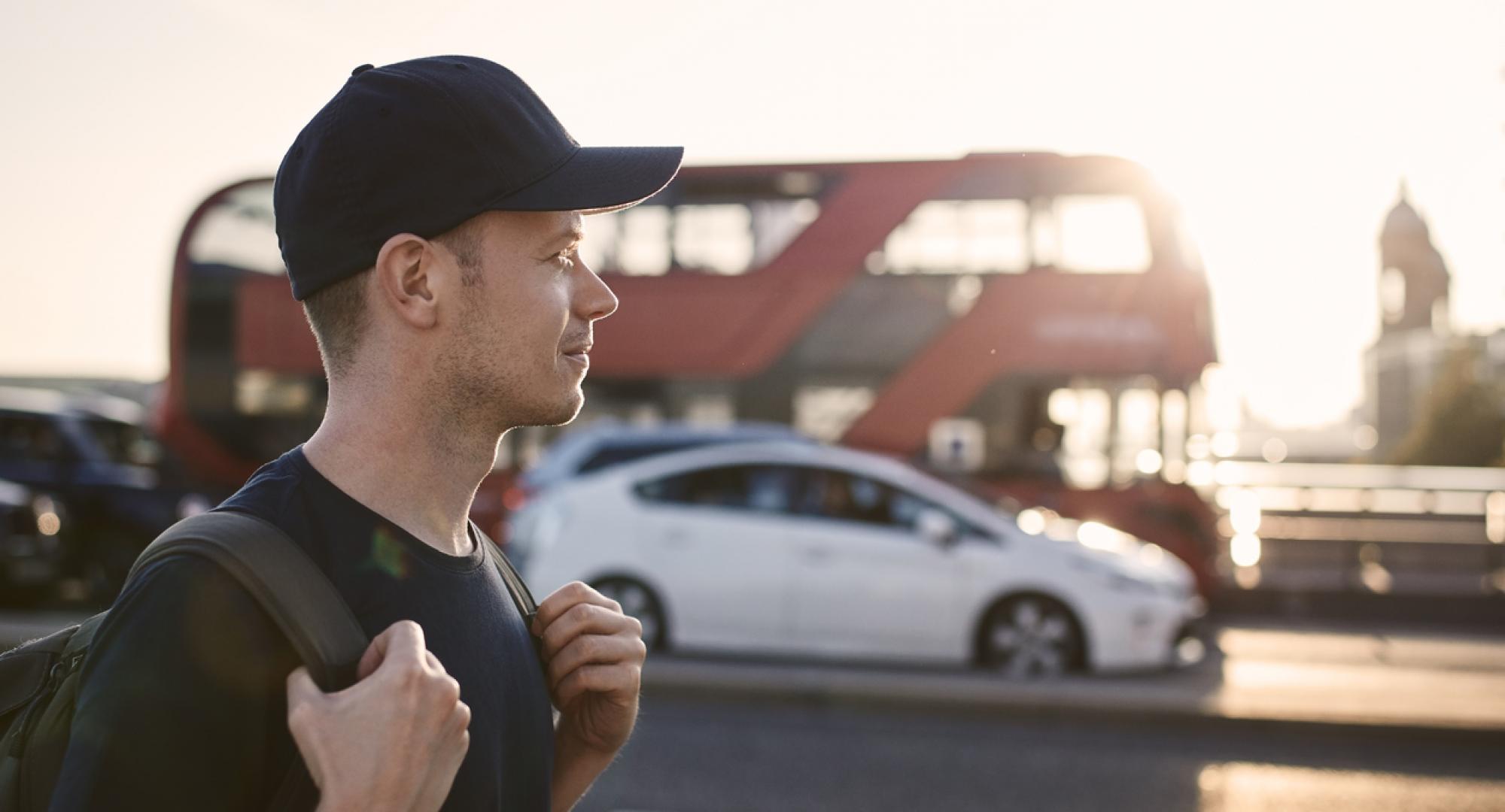 Portrait of cheerful man on city street. Tourist against bus of public transportation at beautiful sunset. London, United Kingdom