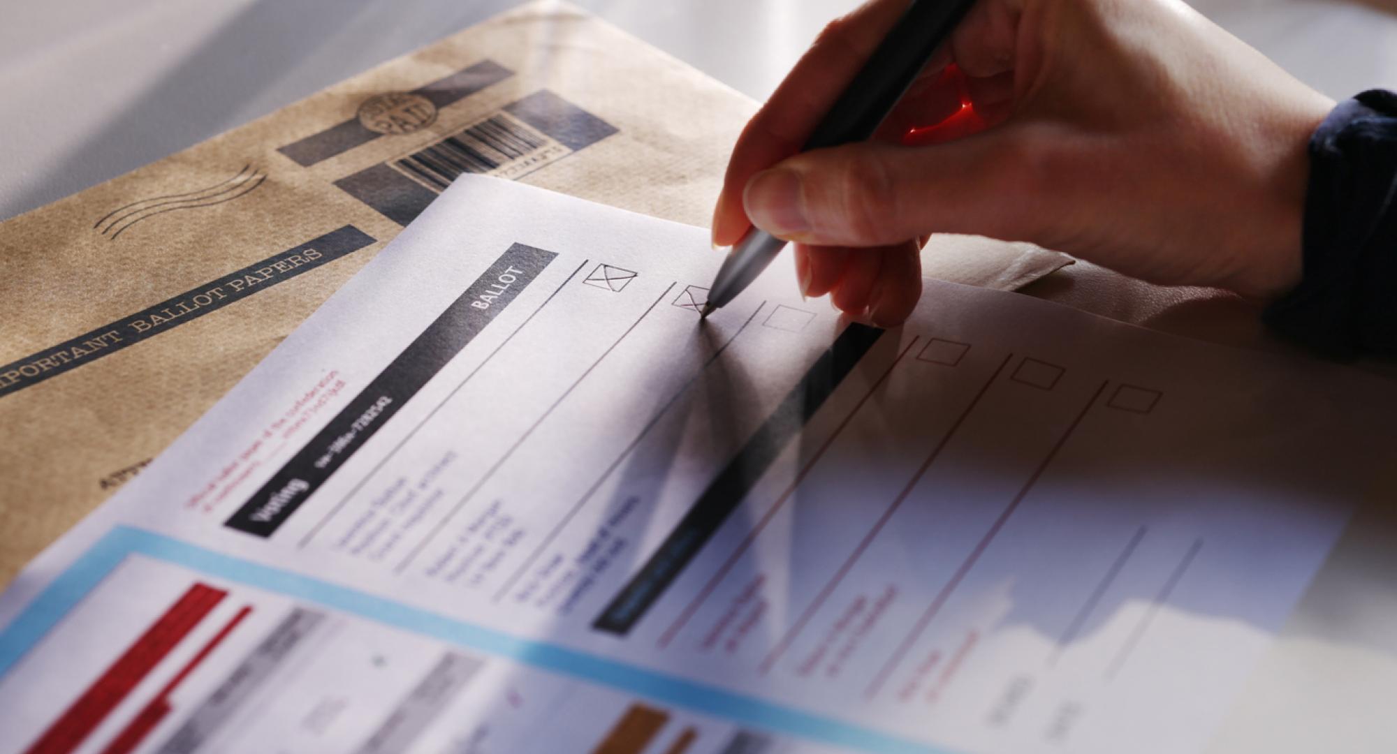 a woman’s hand filling in a postal ballot  voting form.