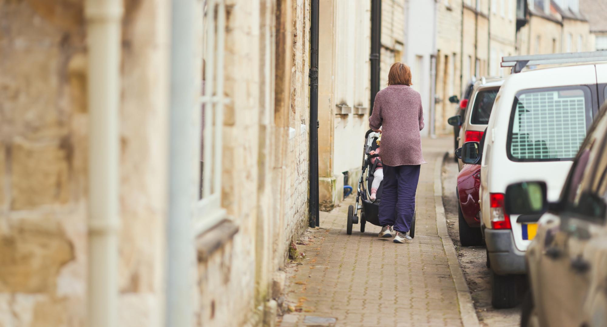 Woman pushing a child along the pavement in a pushchair