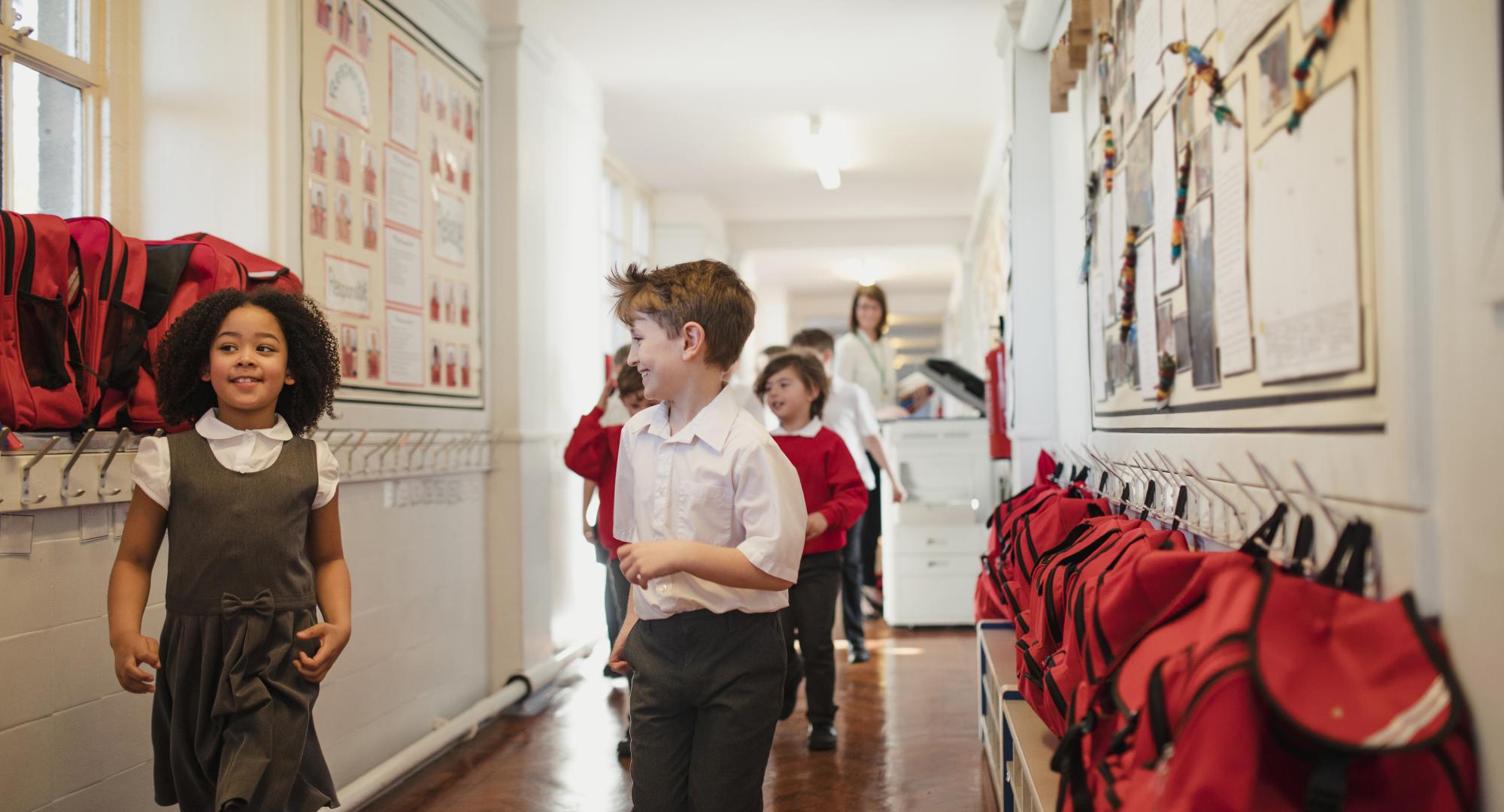 A group of school children wearing uniforms walk through the corridor