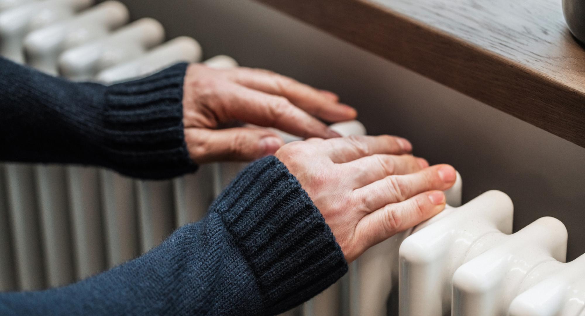 A man tries to warm his hands on a radiator