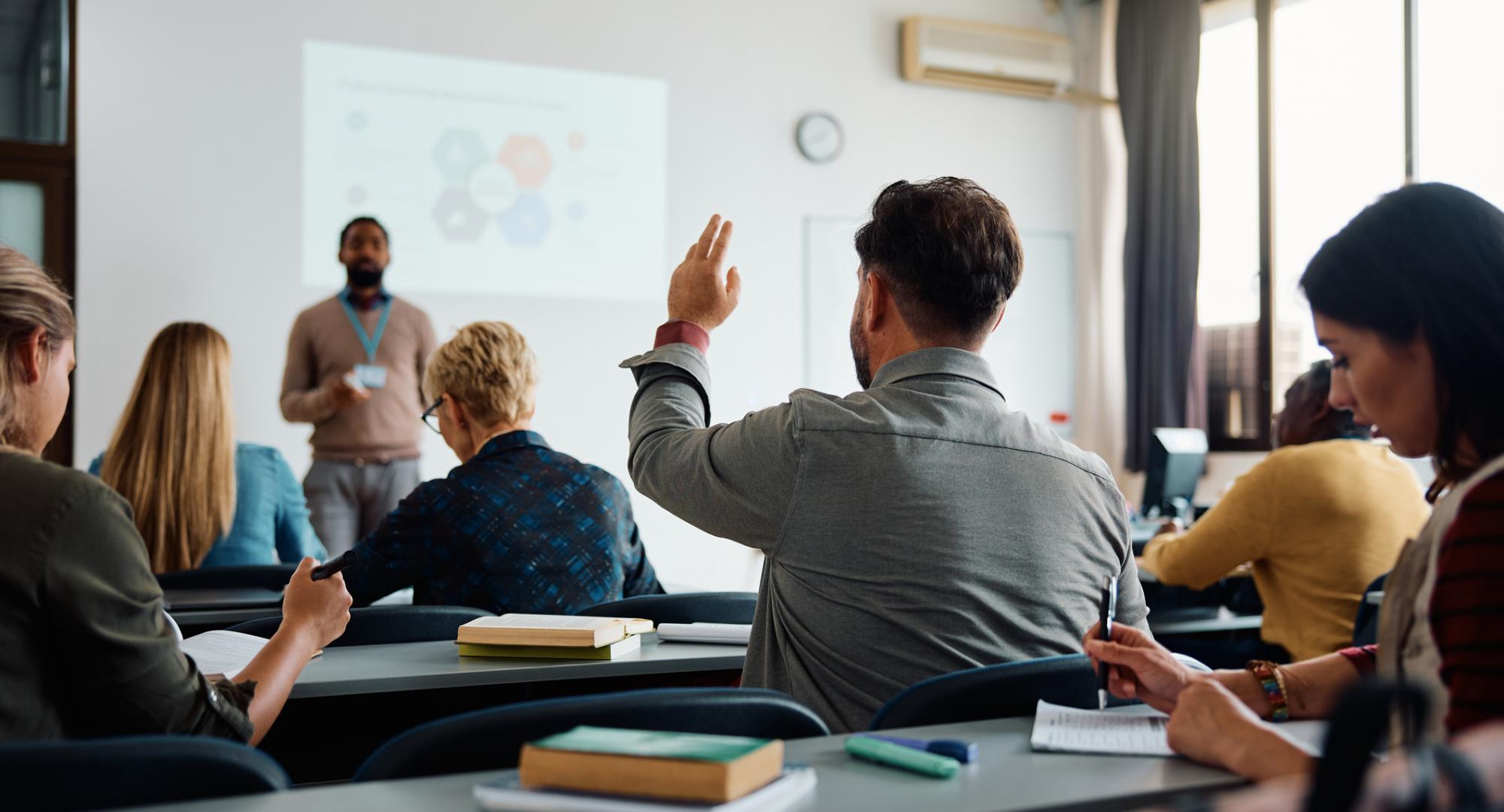 Rear view of man raising arm to ask a question during a presentation