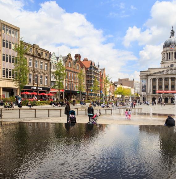 Various people sitting, walking, visiting in the main Market Square, Nottingham Council House building behind.