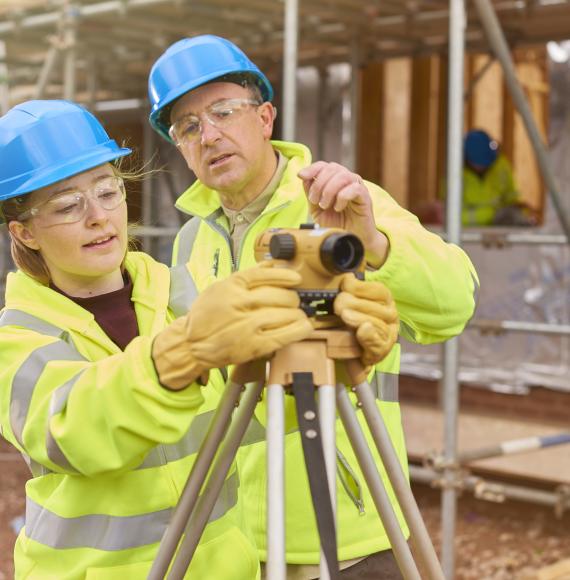 A female construction worker stands behind a builder's level on a building sit