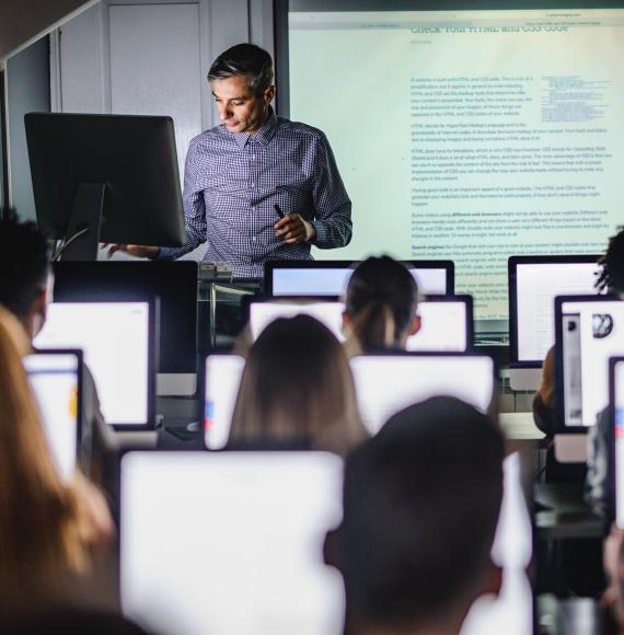 Male teacher giving a lecture from desktop PC during a class at computer lab.