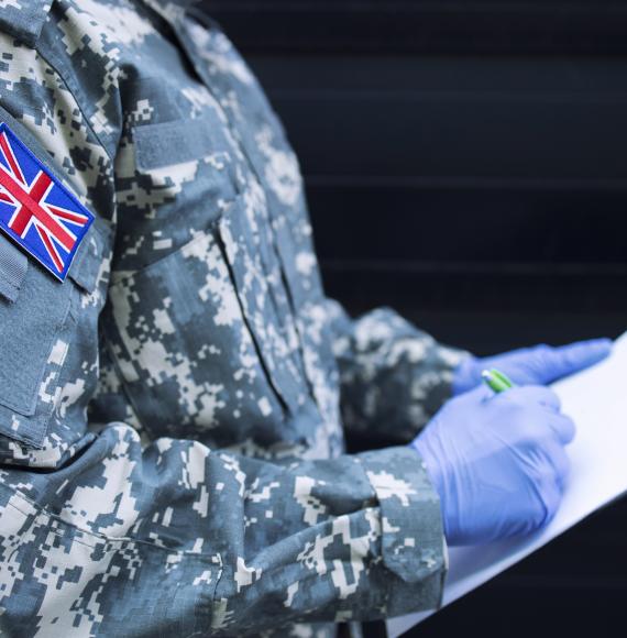 Britain soldier in camouflage uniform with rubber gloves, mask guarding in front of hospital's door controlling who gets in or out.