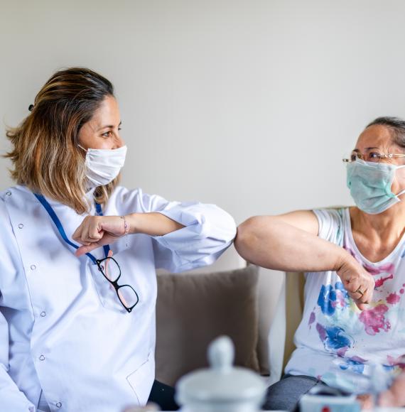 Nurse and patient bumping elbows in a care home, with face coverings on.