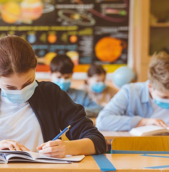 Children working in a classroom, socially distanced with face masks on.