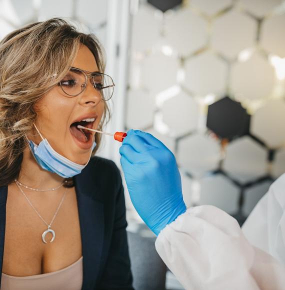 Woman in glasses receives Covid test from man wearing PPE.