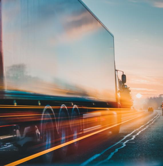 HGV travelling down an A-road, with the sun setting up ahead.