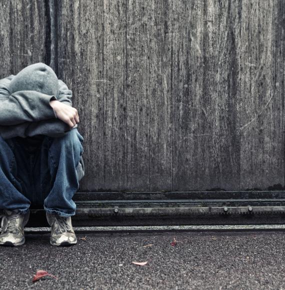 Homeless youth sits on the street looking sad. 