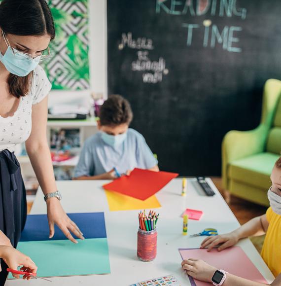 Teacher in a face mask teaches small child.