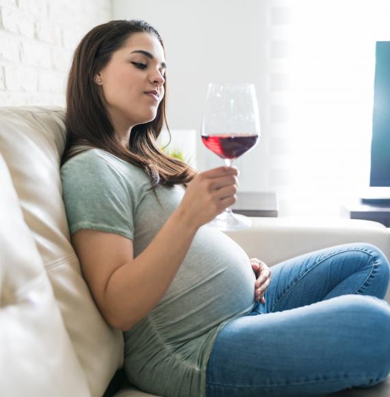 Pregnant woman enjoys glass of wine at home.