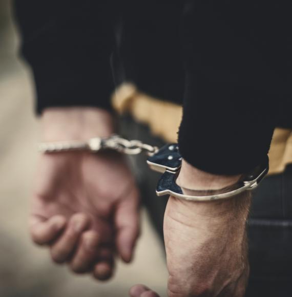 Man with arms behind his back in handcuffs.