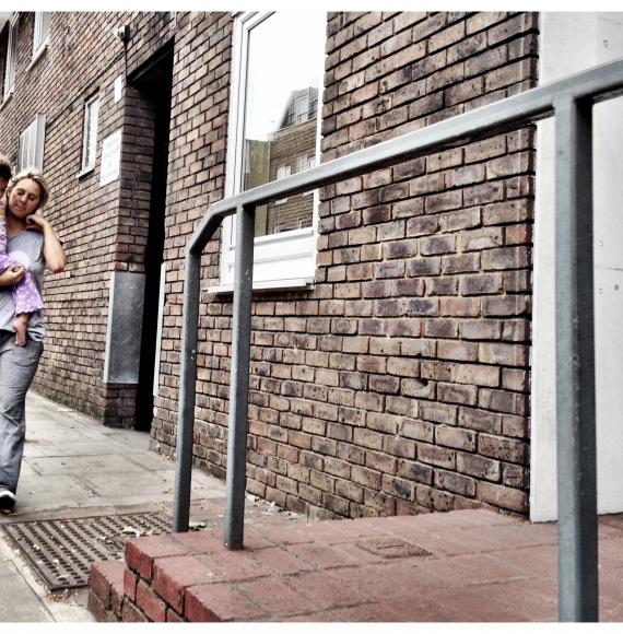 A mother carrying her daughter along the pavement outside a block of council flats 