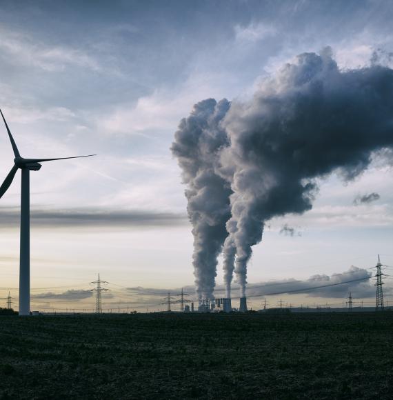 Wind turbine stands in the foreground as coal power station puts steam into atmosphere.