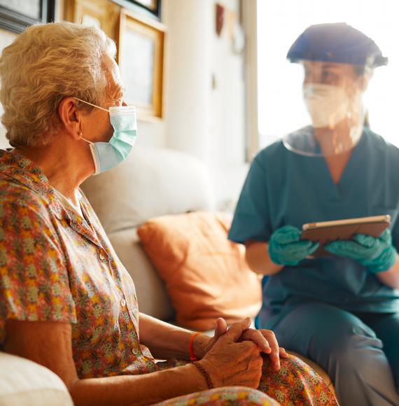 Care home nurse sits with resident in PPE. 