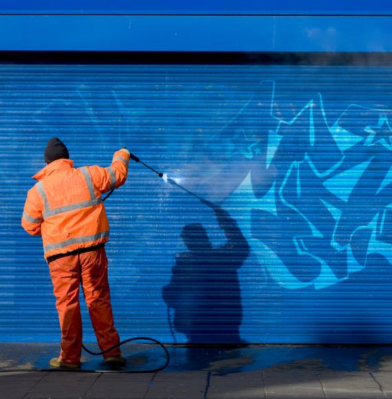 Man removes graffiti from shop front.