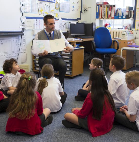 Children sit with teacher as he reads a story.