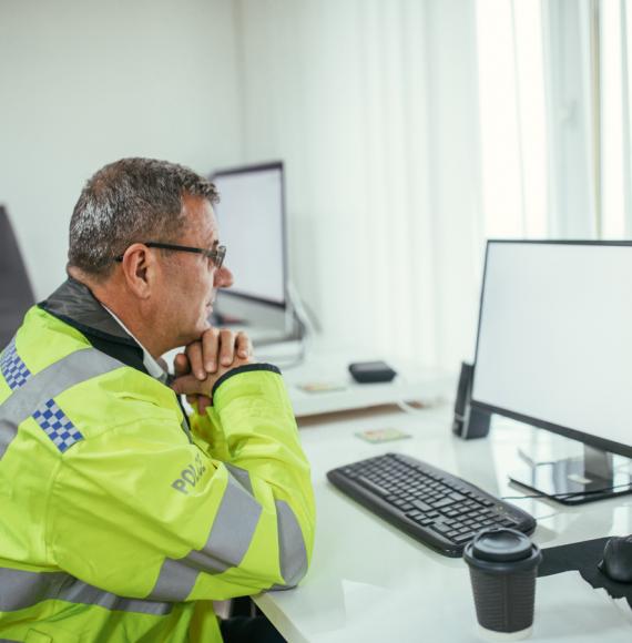 Poliec officer at a desk staring at a computer screen