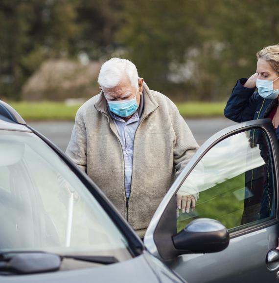 Carer helping elderly man into car