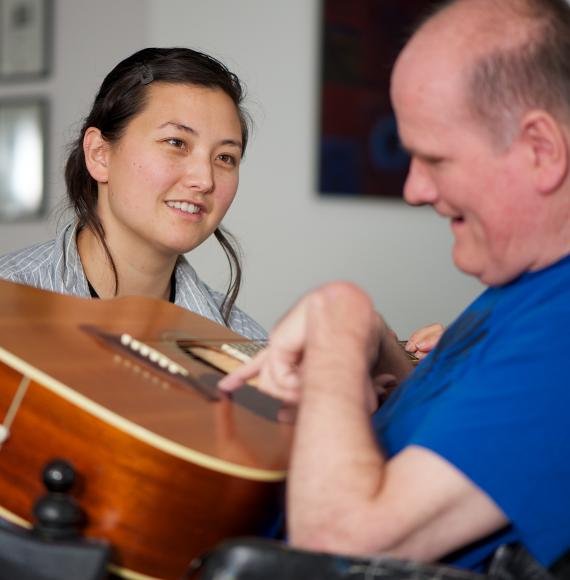 Social care worker sitting with a disabled man as he plays guitar