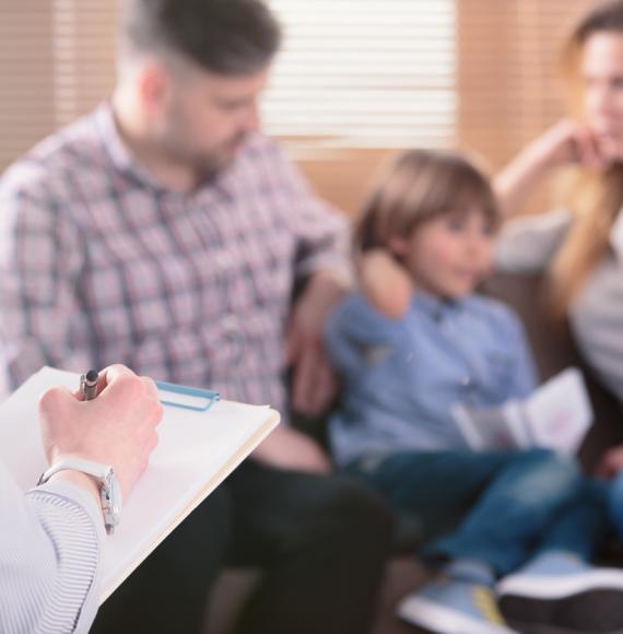 A child sits with two adults as a professional makes notes