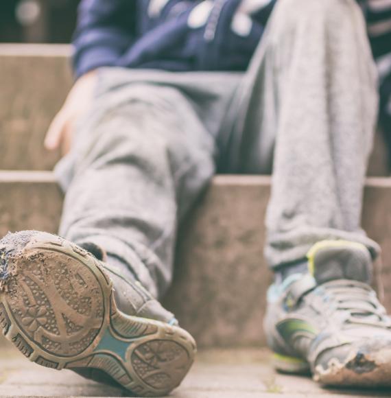 The torn shoes and dirty clothes of a child in poverty