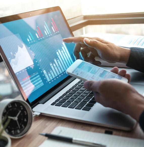 Someone doing business on a laptop and a mobile phone, with a graph on the screen