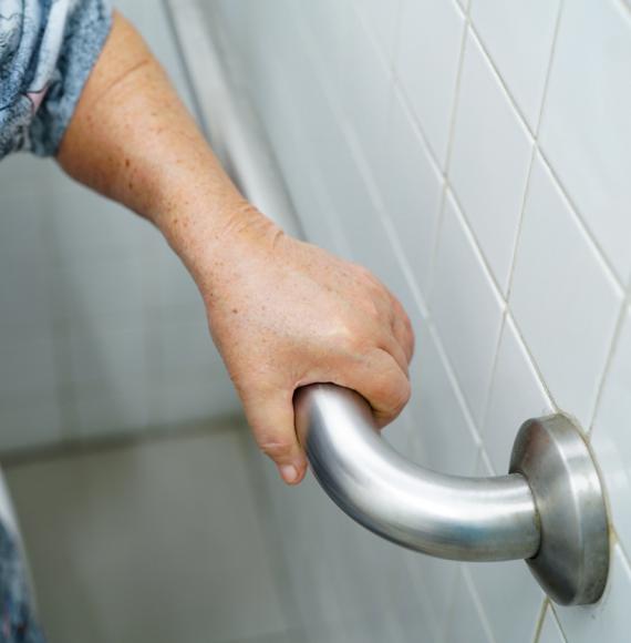 A disabled elderly woman using a handrail to steady herself in the toilet