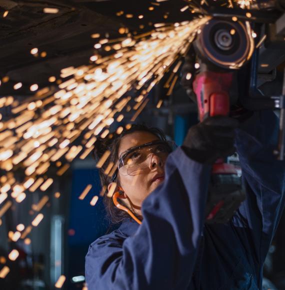 Low angle close up view of a female mechanic using an electric grinder tool on the base of a car while working at a car garage