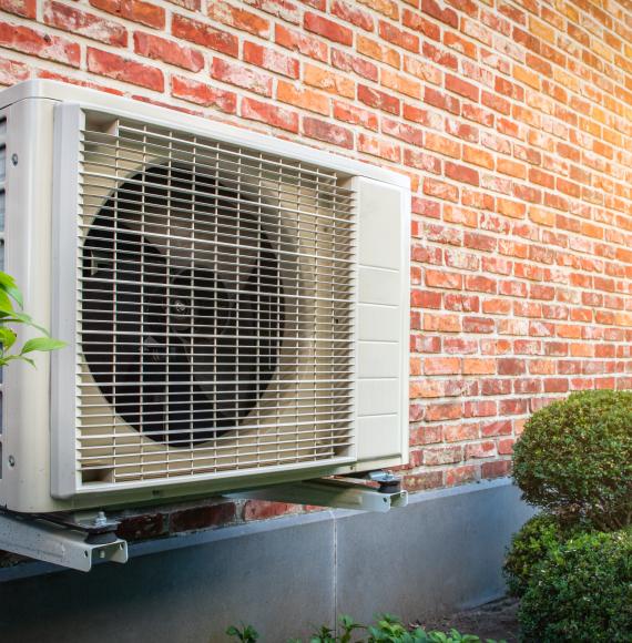 Heat pump outside a home, against a brick wall