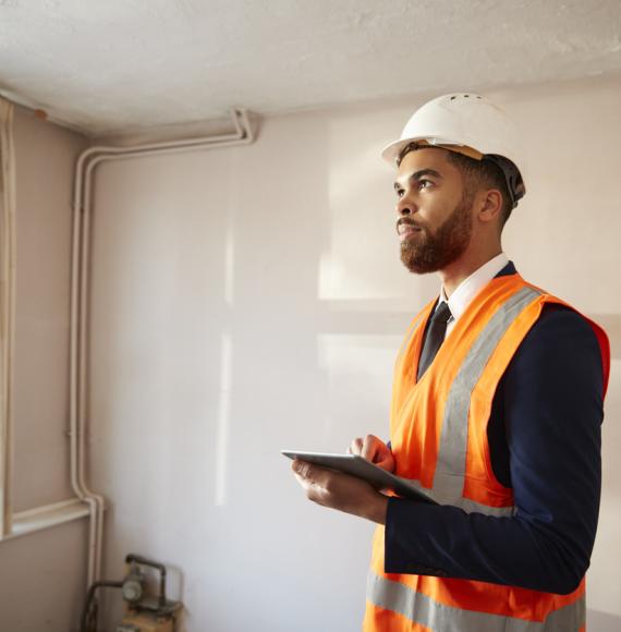 Surveyor In Hard Hat And High Visibility Jacket With Digital Tablet Carrying Out House Inspection